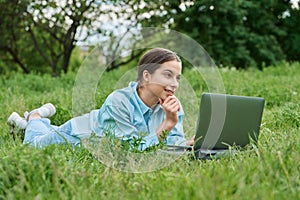 Teenage female student lying on the grass using a laptop