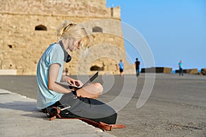 Teenage female tourist using laptop, old european historic fortress background.