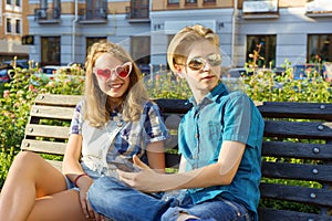 Teenage friends girl and boy sitting on bench in city, talking. Friendship and people concept