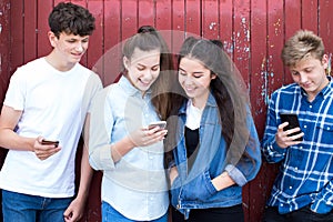 Group Of Teenage Froends Looking At Mobile Phones In Urban Setting