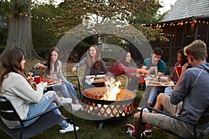 Teenage friends sit round a fire pit eating take-away pizzas