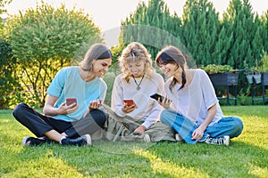 Teenage friends sitting on the grass with smartphones