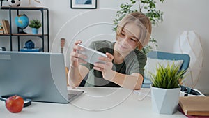 Teenage gamer playing with smartphone touching screen feeling excited enjoying activity at home