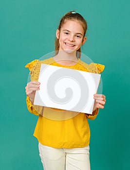 Teenage girl 10 years old in a yellow blouse holding a white sign and smiling on a green background
