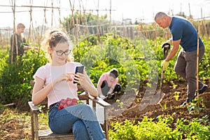 Teenage girl addicting in phone on family vegetable garden