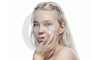 A teenage girl applies cream to her face with freckles. Smiling blonde. Taking care of yourself at a tender age. Close-up. White