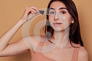 Teenage girl applying cleansing serum against acne and pimples on her cheek. Pretty girl with braces is smiling and holding