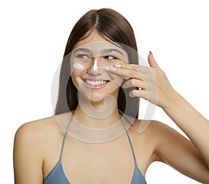 Teenage girl applying sun protection cream on her face against white background