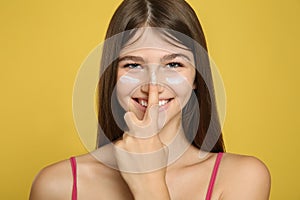 Teenage girl applying sun protection cream on her face against yellow background