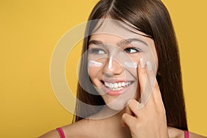 Teenage girl applying sun protection cream on her face against yellow background
