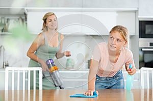 Teenage girl assisting mother in cleaning apartment, wiping kitchen table