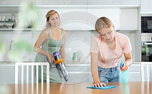 Teenage girl assisting mother in cleaning apartment, wiping kitchen table