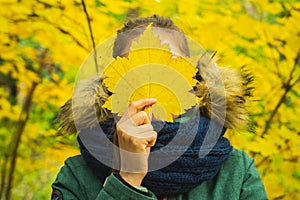 Teenage girl in autumn park covering face with autumn leaf. Selective focus