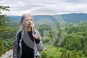 Teenage girl with a backpack walks along the top of the mountain against the backdrop of wooded hills