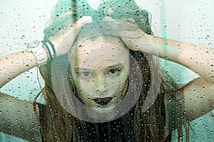 Teenage girl behind window with raindrops tousles her hair