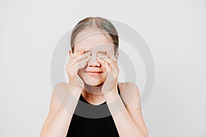 Teenage girl in black T-shirt closes eyes with hands against white wall