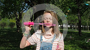 A teenage girl blows bubbles. Girl in the park on a sunny day. A teenage girl is playing with bubbles in the fresh air.