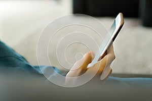 Teenage girl in a blue dress laying on a sofa while holding a smart phone with a blank screen in the hands. Young girl using