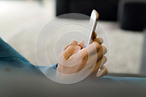 Teenage girl in a blue dress laying on a sofa while holding a smart phone with a blank screen in the hands. Young girl using