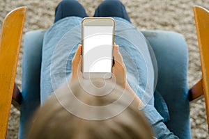 Teenage girl in a blue dress sitting on an armchair while holding a smart phone with a blank screen in the hands. Young girl using