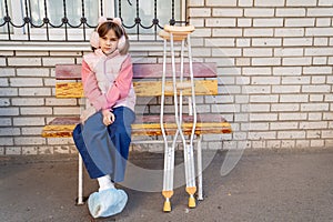 a teenage girl with a broken leg and crutches sits on a bench