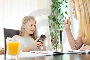 Teenage girl browsing internet on her smart phone while doing homework