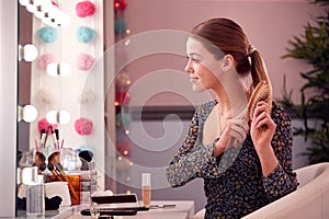 Teenage Girl Brushing Hair In Make Up Mirror In Bedroom At Home