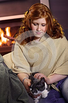 Teenage girl caress cat at home fireplace