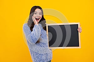 Teenage girl child holding blackboard, isolated on a yellow background. Amazed teenager. Excited teen girl.