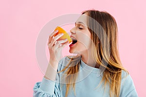 Teenage girl with closed eyes biting orange half isolated on pink