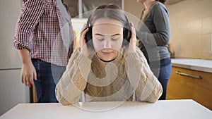 Teenage girl closing ears with headphones while parents argue, shout and scream on the background. Family violence