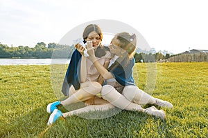 Teenage girl comforts her crying, upset, sad friend. The girls are sitting on the green grass in the park