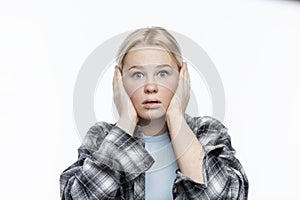 A teenage girl covered her ears with her hands. Cute blonde girl with freckles on her face wearing a plaid shirt. White background