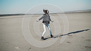 A teenage girl dances in a black jacket in the open air.. Hair in the wind.