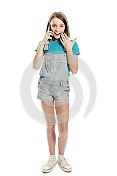 A teenage girl in denim overalls and a blue T-shirt emotionally talks on a smartphone. Communication and technology. Isolated on a