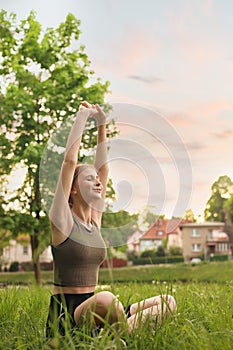 Teenage girl doing morning exercise on green grass in park