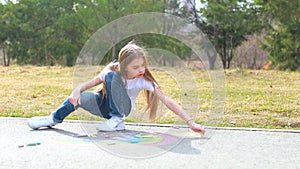 teenage girl drawing a rainbow colored chalk on the asphalt on summer day