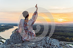 teenage girl in dress, with short-cropped hair, on top cliff, on river bank, at sunset