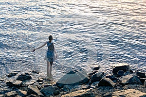 Teenage girl in a dress stands in the water near the shore and enjoys the morning sun