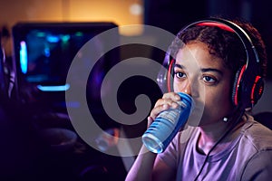 Teenage Girl Drinking Caffeine Energy Drink Gaming At Home Using Dual Computer Screens At Night photo