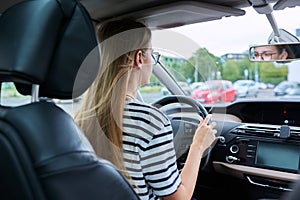 Teenage girl driver in glasses sitting behind wheel of car
