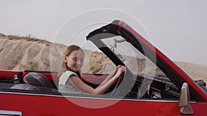 Teenage girl driving red cabriolet against sky during windy day