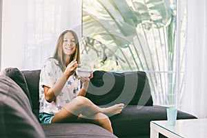 Teenage girl eating brekfast on couch in living room
