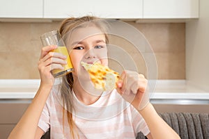 Teenage girl eating a slice of pizza and drinking orange juice in the kitchen