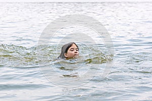 A teenage girl enjoys swimming in the calm warm lake water in beautiful summer weather