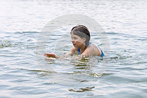 A teenage girl enjoys swimming in the calm warm lake water in beautiful summer weather