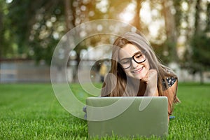 Teenage girl in eyeglasses looking at the notebook outdoors