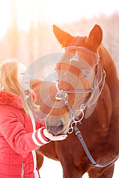 Teenage girl feeding bay horse on winter field