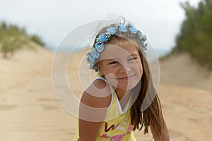 Teenage girl in a flower wreath on her head sitting on the Golden sand on the beach