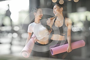 A teenage girl friend is walking holding a purple yoga mats after giving up yoga on the gym blurry foreground, A photo through a